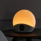 Restli Rise väckarklocka med rund ljuskupa som lyser varmt orange och en digital display i den grå textilfoten